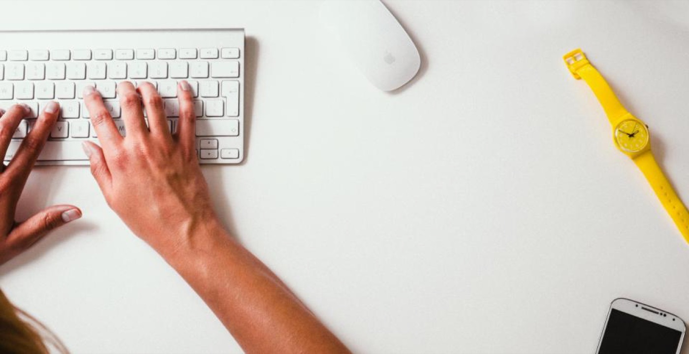 Hands typing on a keyboard beside a yellow watch